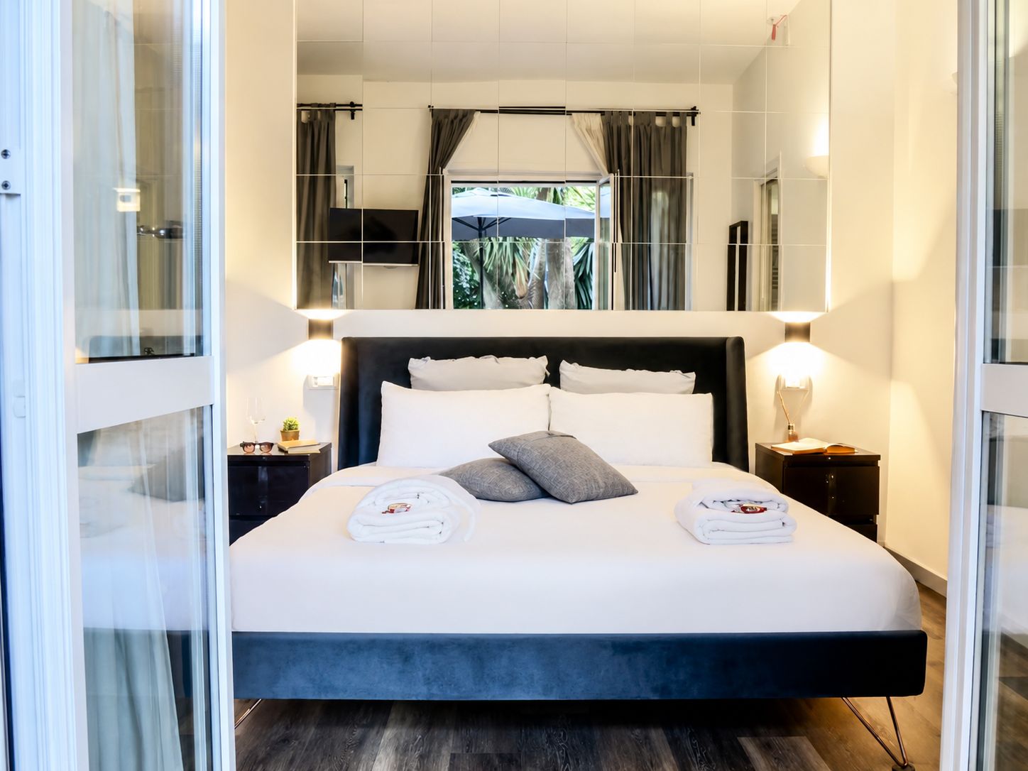Moderni hotellihuone, jossa on suuri sänky, yöpöytävalaisimet, näkymä ulos ja lasinen sermi.
