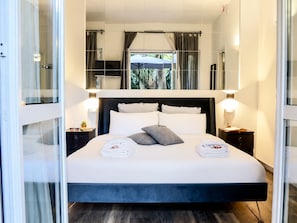 Quarto de hotel moderno com uma cama grande, abajures, vista para o exterior e um painel de vidro.