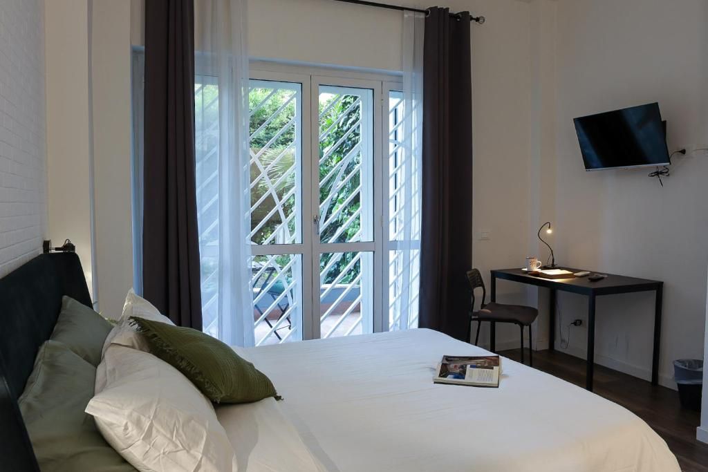 Une chambre à coucher comprenant un lit, un bureau, une chaise, un téléviseur et une fenêtre avec des rideaux.