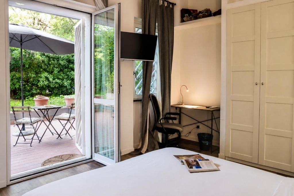 Une chambre avec un lit, un bureau, une chaise et un téléviseur. Une porte-fenêtre coulissante donne accès à un espace extérieur aménagé avec une table et des chaises.