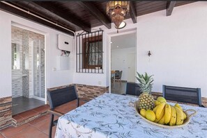 Ein Essbereich mit einem Tisch für zwei Personen, einer Obstschale mit Bananen und einer Ananas sowie Blick auf eine Glastür, die zu einer Terrasse führt.