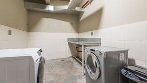 Une buanderie équipée de deux machines à laver, d’un évier et de murs carrelés.