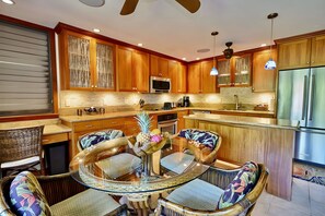Una cocina moderna con armarios de madera, una isla central y una zona de comedor con sillas de mimbre.