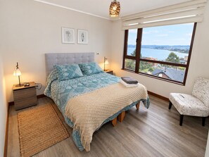 Ein Schlafzimmer mit einem Bett, Nachttischen, einem Fenster mit Aussicht und einem Sessel.