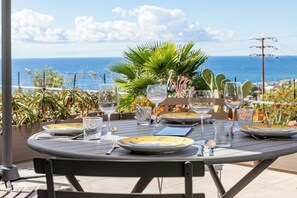 Un tavolo da pranzo all'aperto con piatti, bicchieri e posate, con vista sul mare e sulla vegetazione.