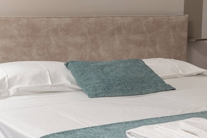 Ein Bett mit weißer Bettwäsche und einem türkisblauen Zierkissen.