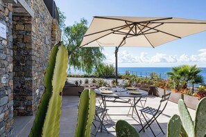 Un patio esterno con tavolo e sedie, un ombrellone grande e vista sul mare.