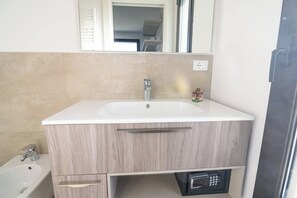 Un baño con un lavamanos blanco, un espejo encima y un inodoro a la izquierda.