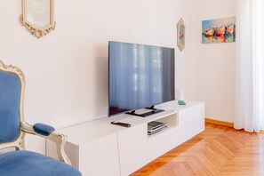 Uma sala de estar moderna com uma TV de tela plana sobre um armário branco, uma poltrona azul e uma pintura na parede.