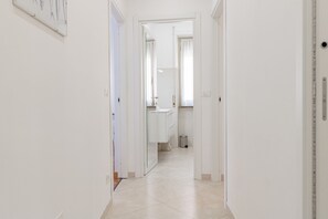 Corredor que dá para um banheiro com vaso sanitário, pia e espelho.