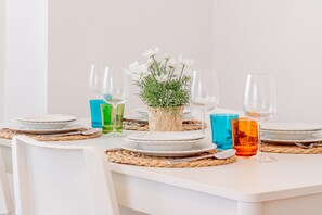 Mesa de jantar posta com pratos, copos e um arranjo central de flores brancas e folhagem.