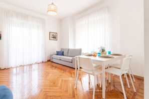 Ein helles Zimmer mit Holzboden, weißen Möbeln und einem Esstisch für zwei Personen.