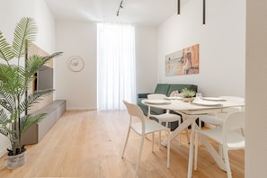 Ein modernes Wohnzimmer mit Essbereich, einer großen Küstertopf-Pflanze, einer Couch und einem Gemälde an der Wand.