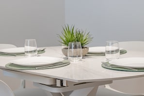 Een gedekte tafel met borden, bestek en glazen, in het midden een potplant.