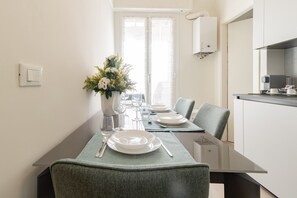 A modern dining area with a glass table, grey upholstered chairs, and a vase of flowers. - ACQUAMARINA - Centro (Sanremo)