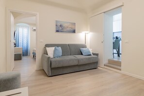 A modern living room with a grey sofa, a painting on the wall, and a staircase leading to another room. - ACQUAMARINA - Centro (Sanremo)