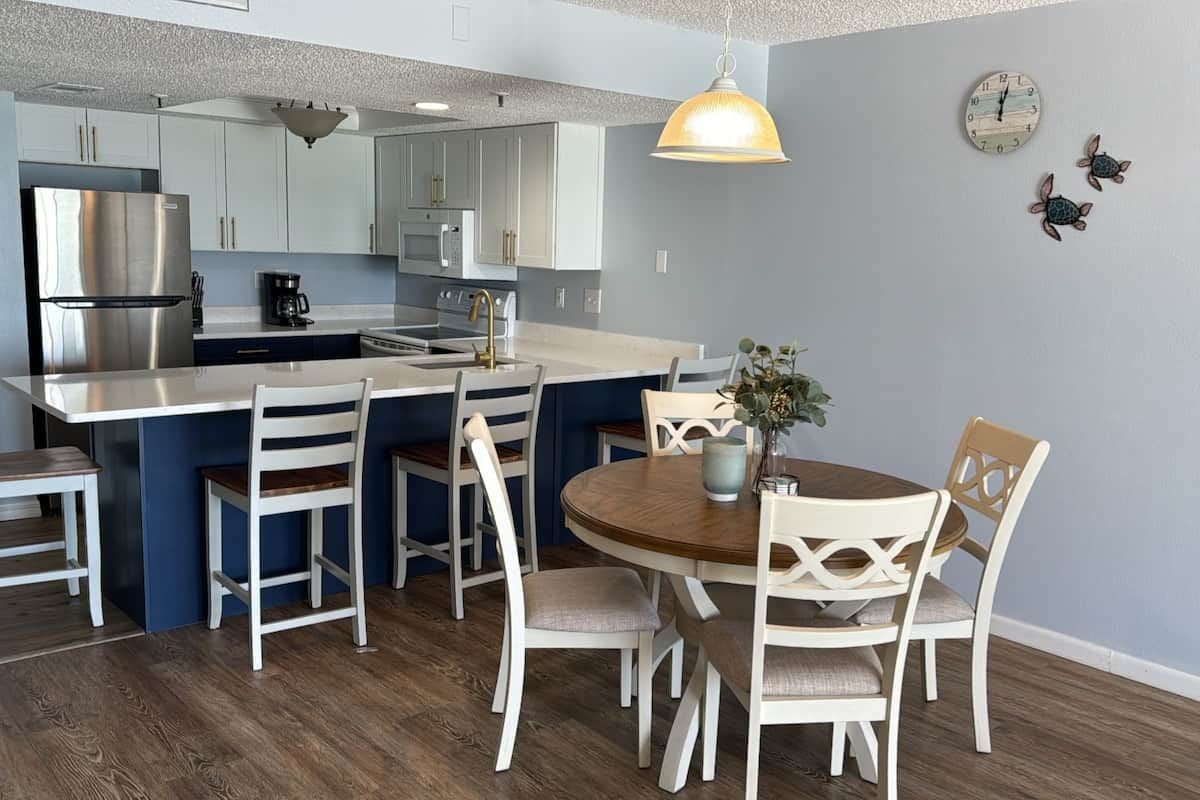 A modern kitchen with white cabinetry, a stainless steel refrigerator, and a round dining table with white chairs.