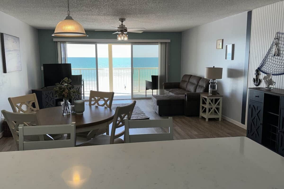 A modern living room with a dining area, a sofa, and a view of the ocean.