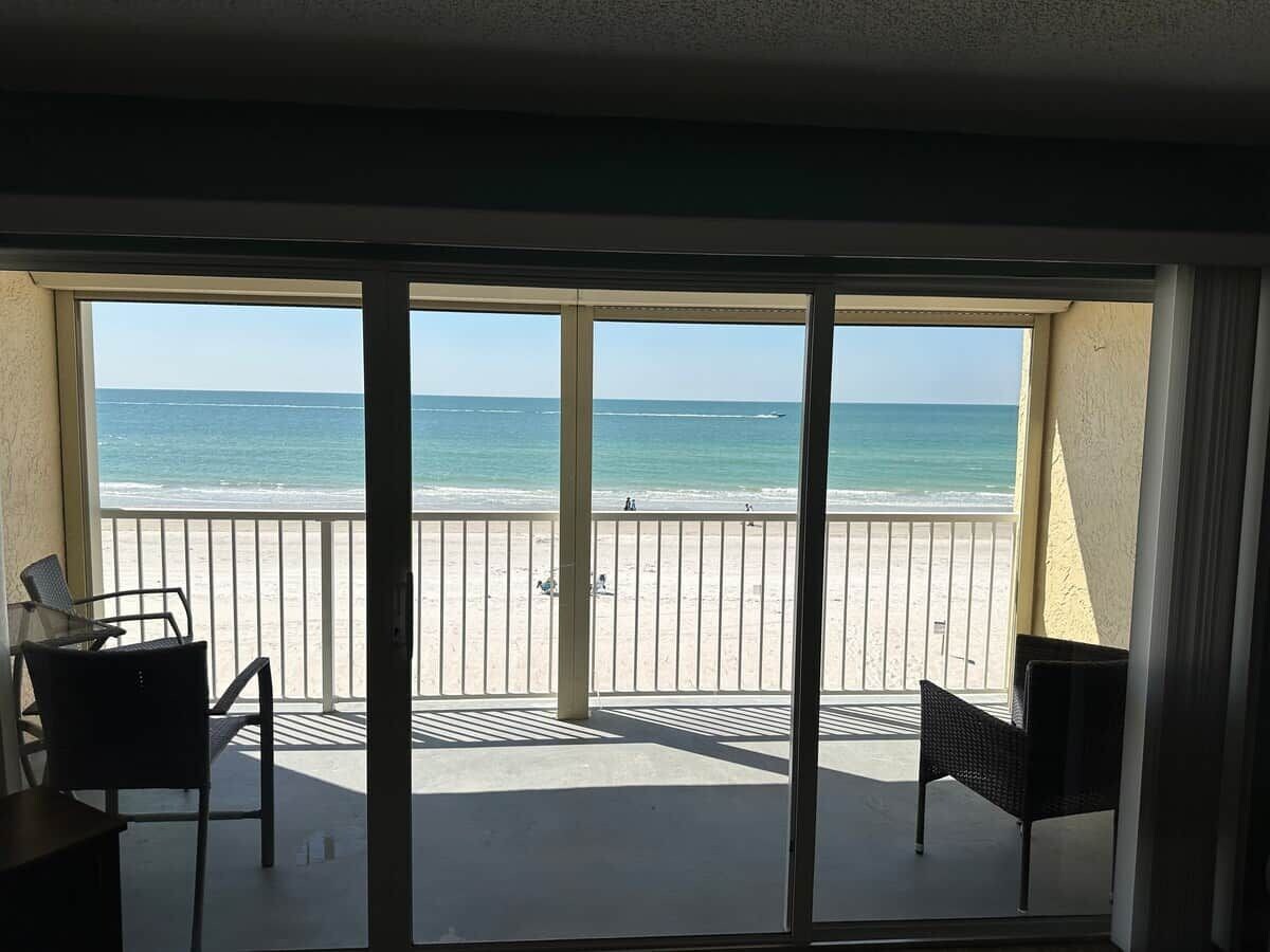 A room with a view of a beach, a sliding glass door, and two chairs.
