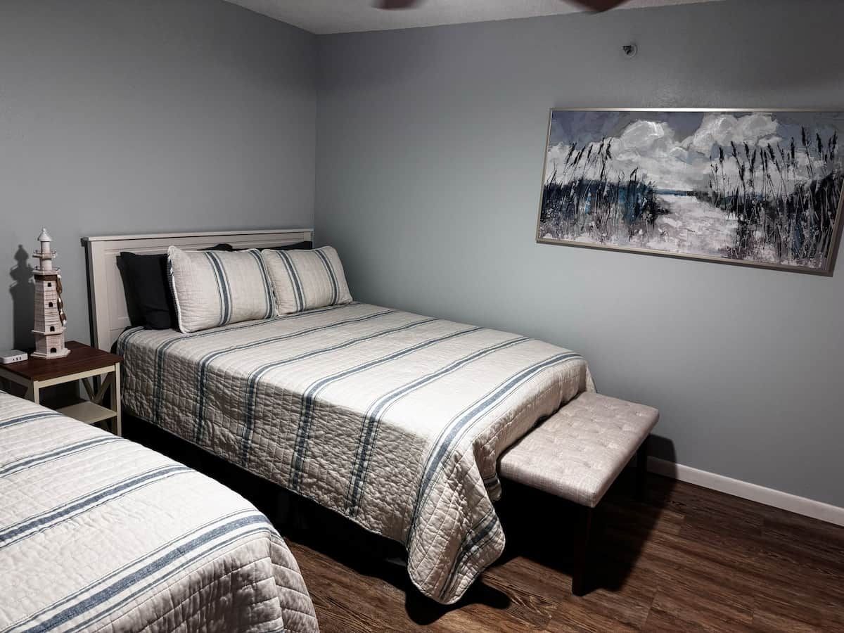 A bedroom with a bed, a bench, a nightstand, and a painting on the wall.