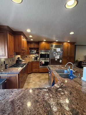 A kitchen with wooden cabinets, a gas stove, a microwave, an oven, a refrigerator, and a granite countertop. - Wasatch Chalet - 3BR Sandy Mountain Retreat (Sandy)