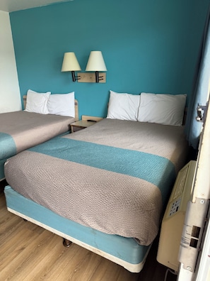 Una cama doble con una colcha estampada, una mesita de noche con lámpara y una lámpara de pared.