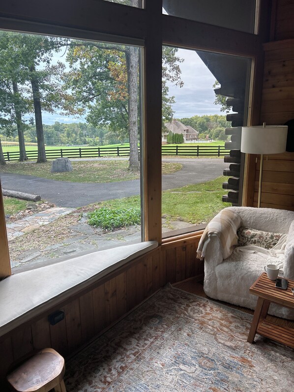 A cozy room with a large window, a plush sofa, a small table with a cup and a smartphone, and a wooden floor.