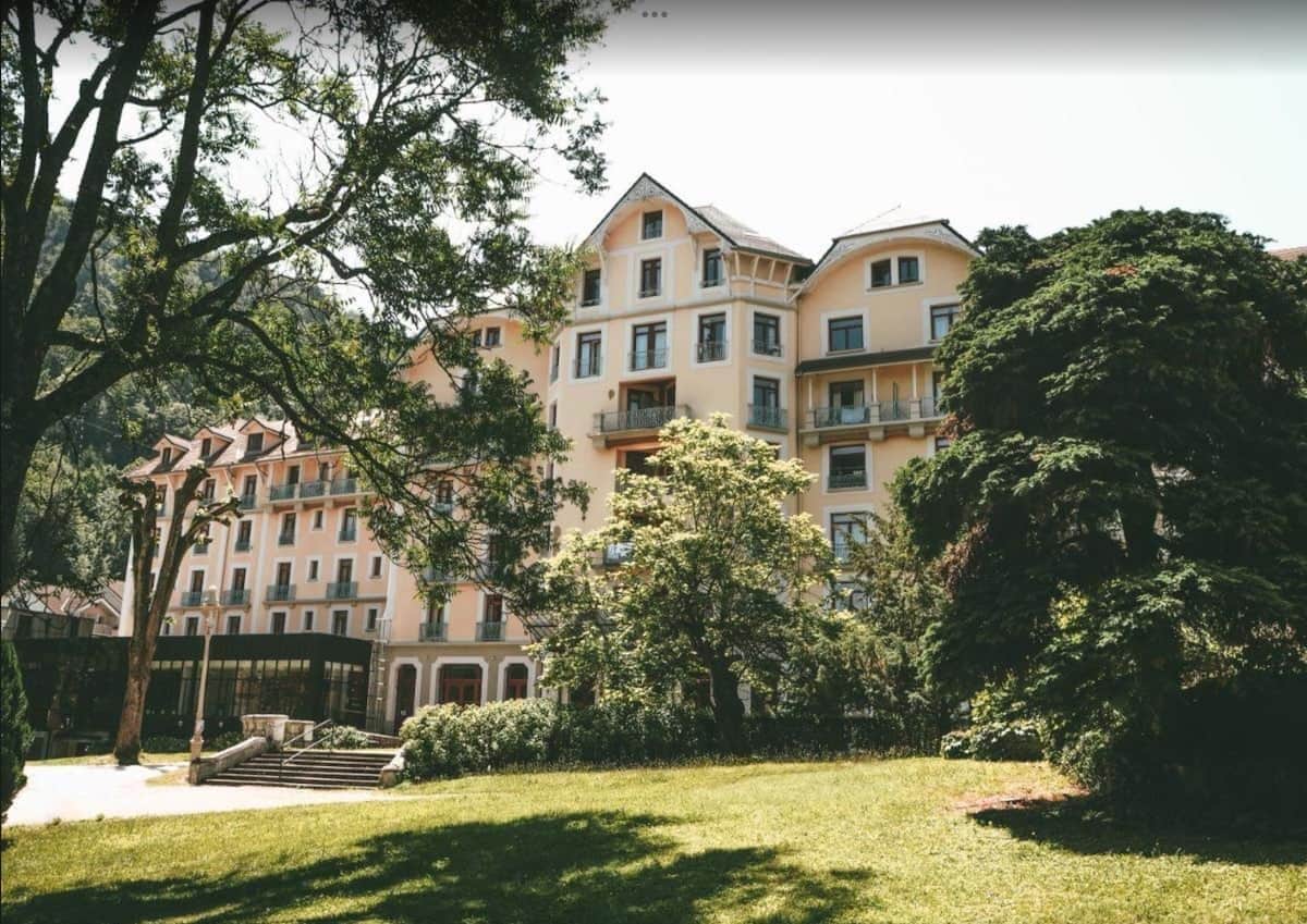 A multi-story hotel with a central courtyard, surrounded by lush greenery and trees.