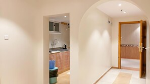 A hallway with a kitchen area, a trash bin, and a wooden door. - REFAD PLUS Ahad rufaidah (Al Khaleej District,Ahad Rafidah)