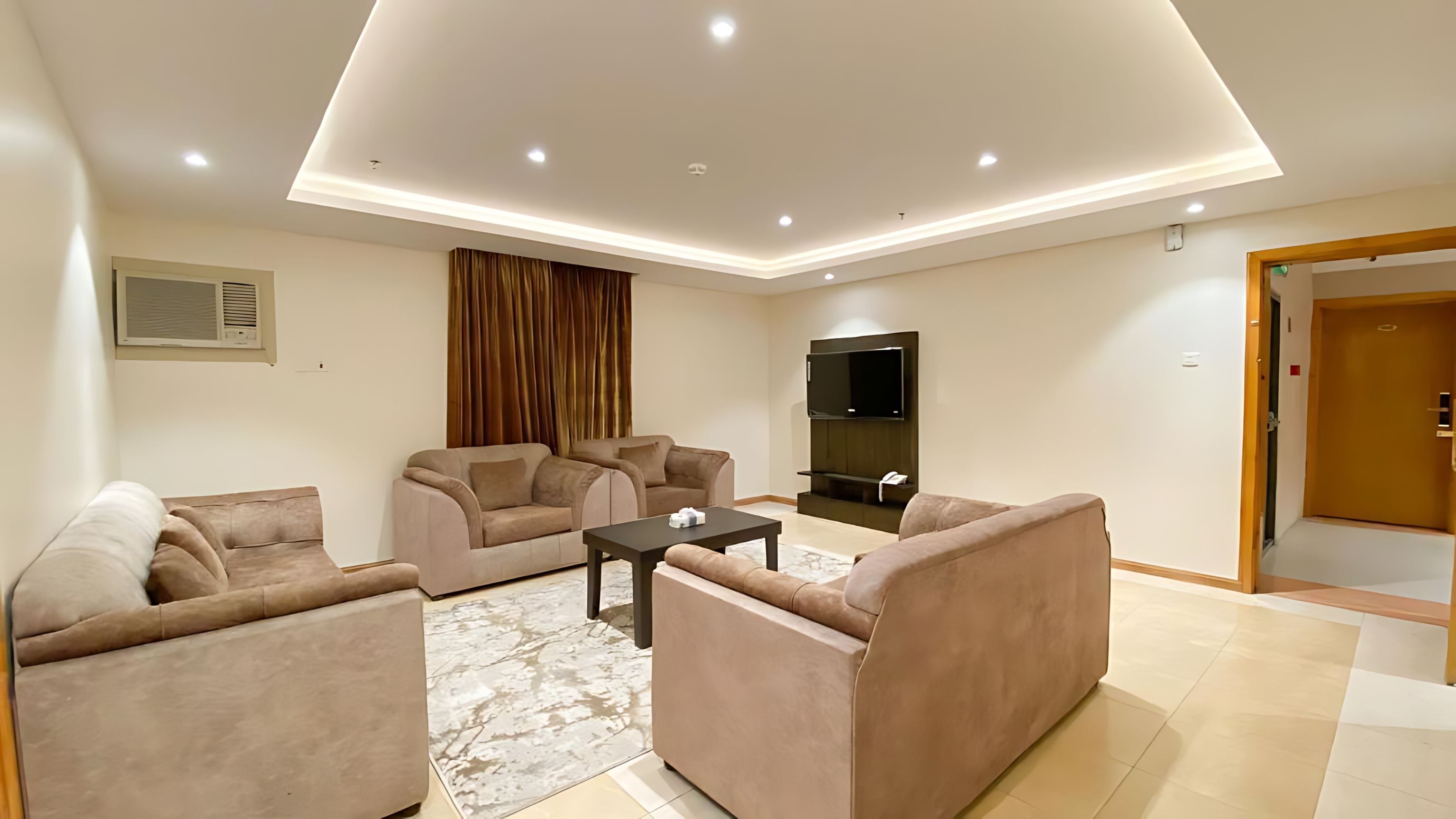 A modern living room with a flat-screen TV, two sofas, a coffee table, and a patterned rug.