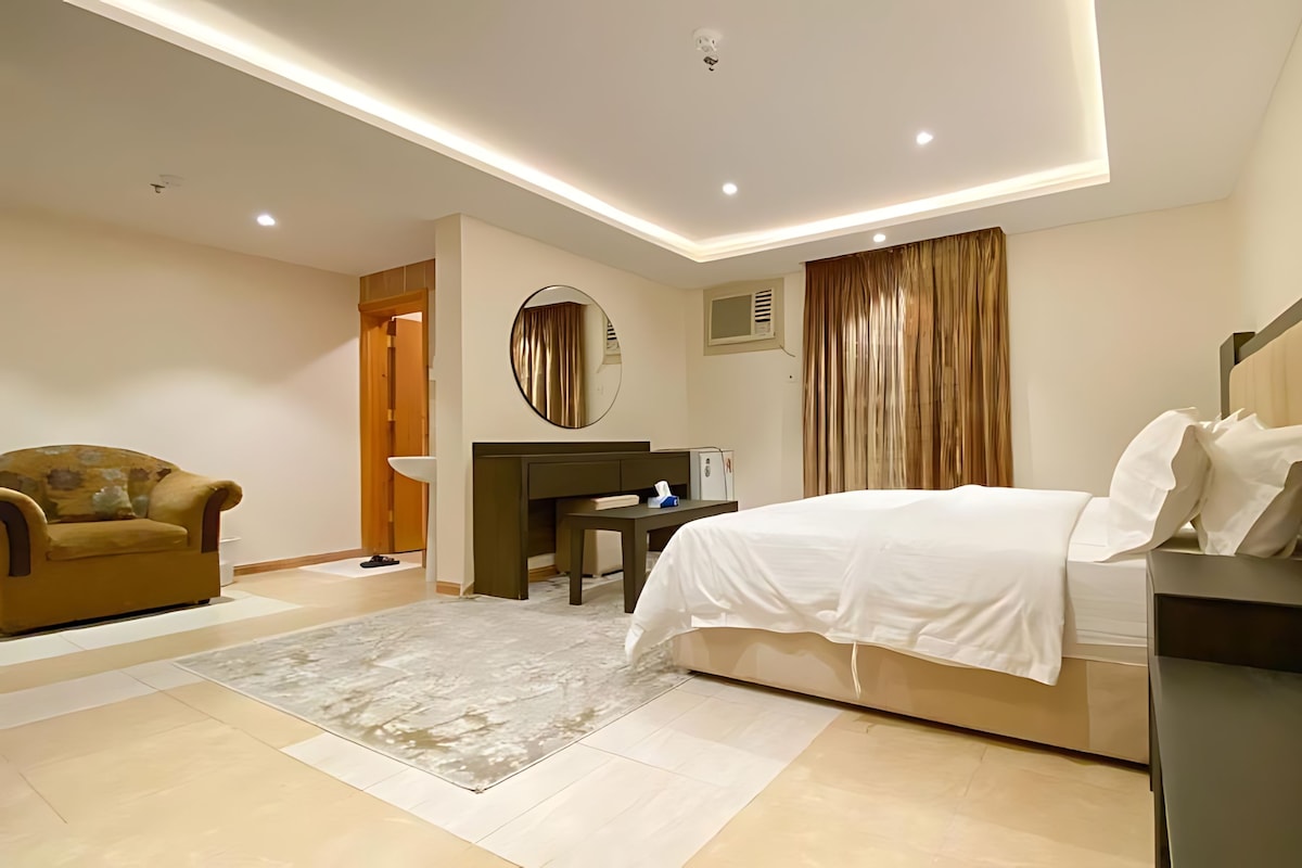 A modern hotel room with a bed, a desk, a chair, and a large mirror.