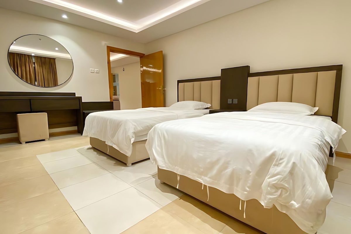 A modern bedroom with two beds, a large mirror, and a wooden headboard.