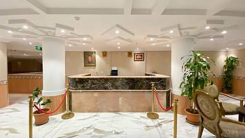 A hotel reception area with marble flooring, a reception desk, and potted plants.