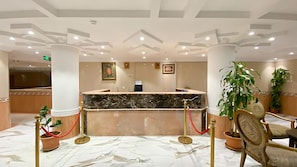 A hotel reception area with marble flooring, a reception desk, and potted plants. - REFAD PLUS Ahad rufaidah (Al Khaleej District,Ahad Rafidah)