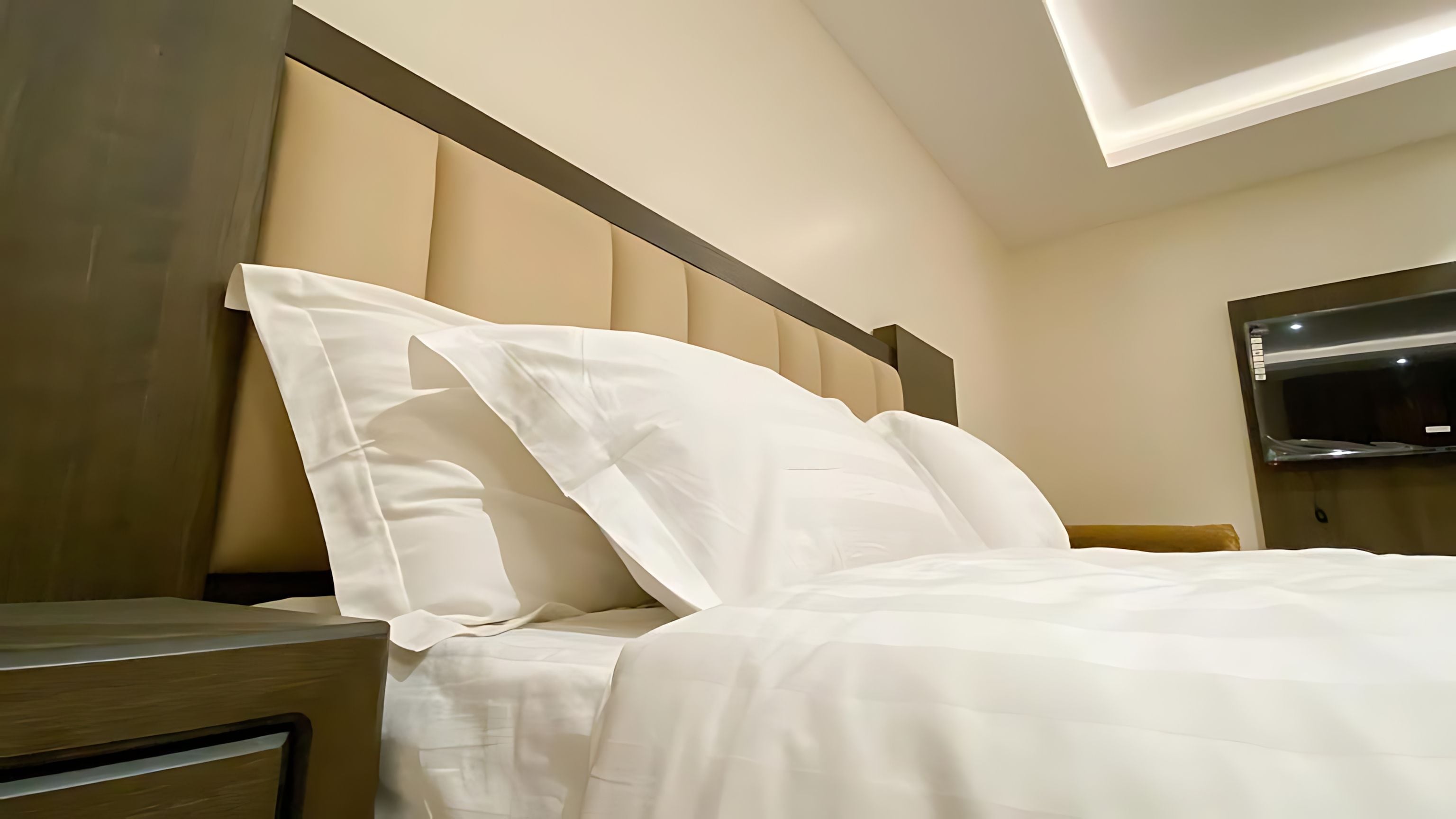 A hotel room with a bed, a nightstand, a flat-screen TV mounted on the wall, and a ceiling light fixture.
