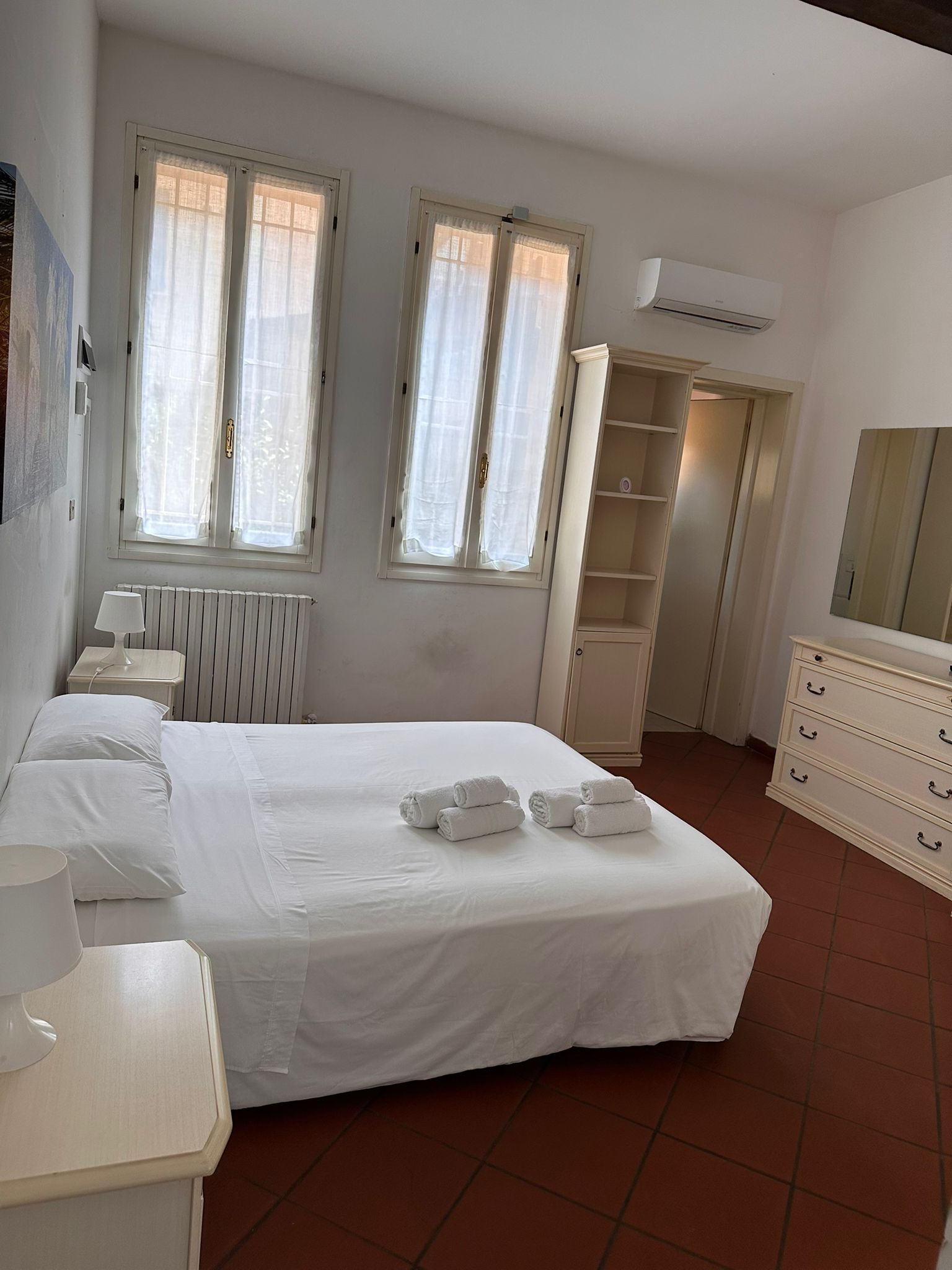 A bedroom with a bed, a dresser, a radiator, and a window with curtains.