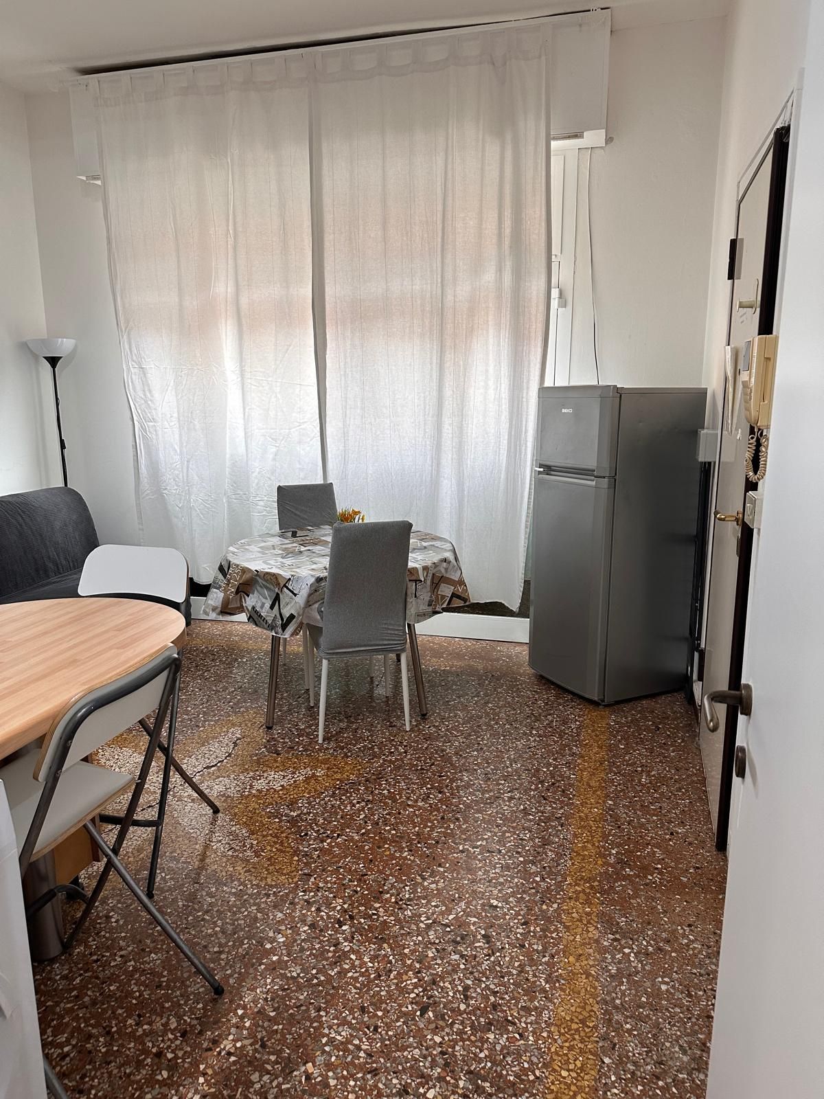Une pièce de taille modeste comprenant une table et des chaises, un petit réfrigérateur et un lit.