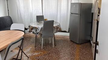 A compact room with a dining table and chairs, a small refrigerator, and a bed.