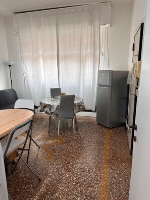 Une pièce de taille modeste comprenant une table et des chaises, un petit réfrigérateur et un lit.