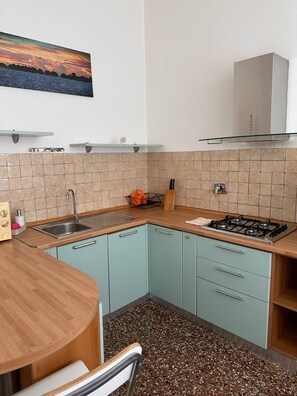 Une cuisine de taille réduite avec des meubles de couleur turquoise, un plan de travail en bois, une cuisinière à gaz et un évier.