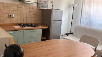 A compact kitchen with a gas stove, a refrigerator, and a dining area with a table and chairs.
