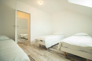 Ein Schlafzimmer mit drei nebeneinander stehenden Betten, Holzboden und einer Tür zu einem anderen Raum.