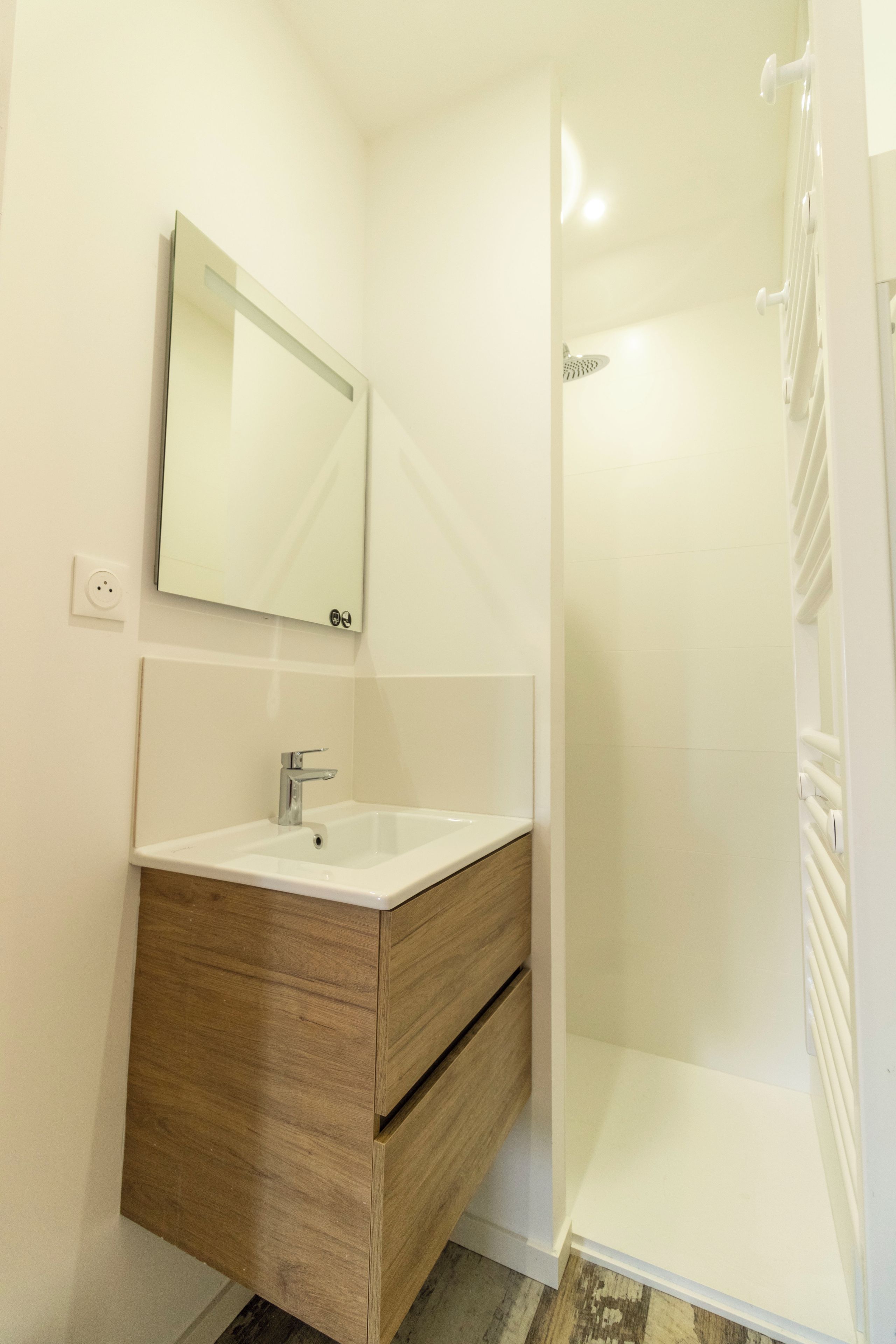 A bathroom with a white sink, wooden vanity, and a shower enclosure.