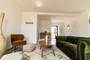 Ein Wohnzimmer mit einem braunen Sessel, einem grünen Sofa, einem runden Couchtisch aus Holz und einer weißen Vase mit Blumen.