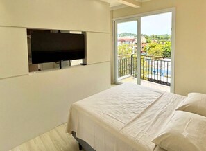 Quarto com cama, televisão fixada na parede e varanda com vista para o exterior.
