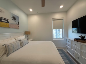 A bedroom with a bed, a nightstand, a lamp, a dresser, a television, and a window. - Las Olas 304 -  Exclusive 3br Condo South Padre Island - Steps from the Sand (South Padre Island)