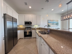 A modern kitchen with white cabinets, stainless steel appliances, granite countertops, and pendant lighting. - Las Olas 304 -  Exclusive 3br Condo South Padre Island - Steps from the Sand (South Padre Island)