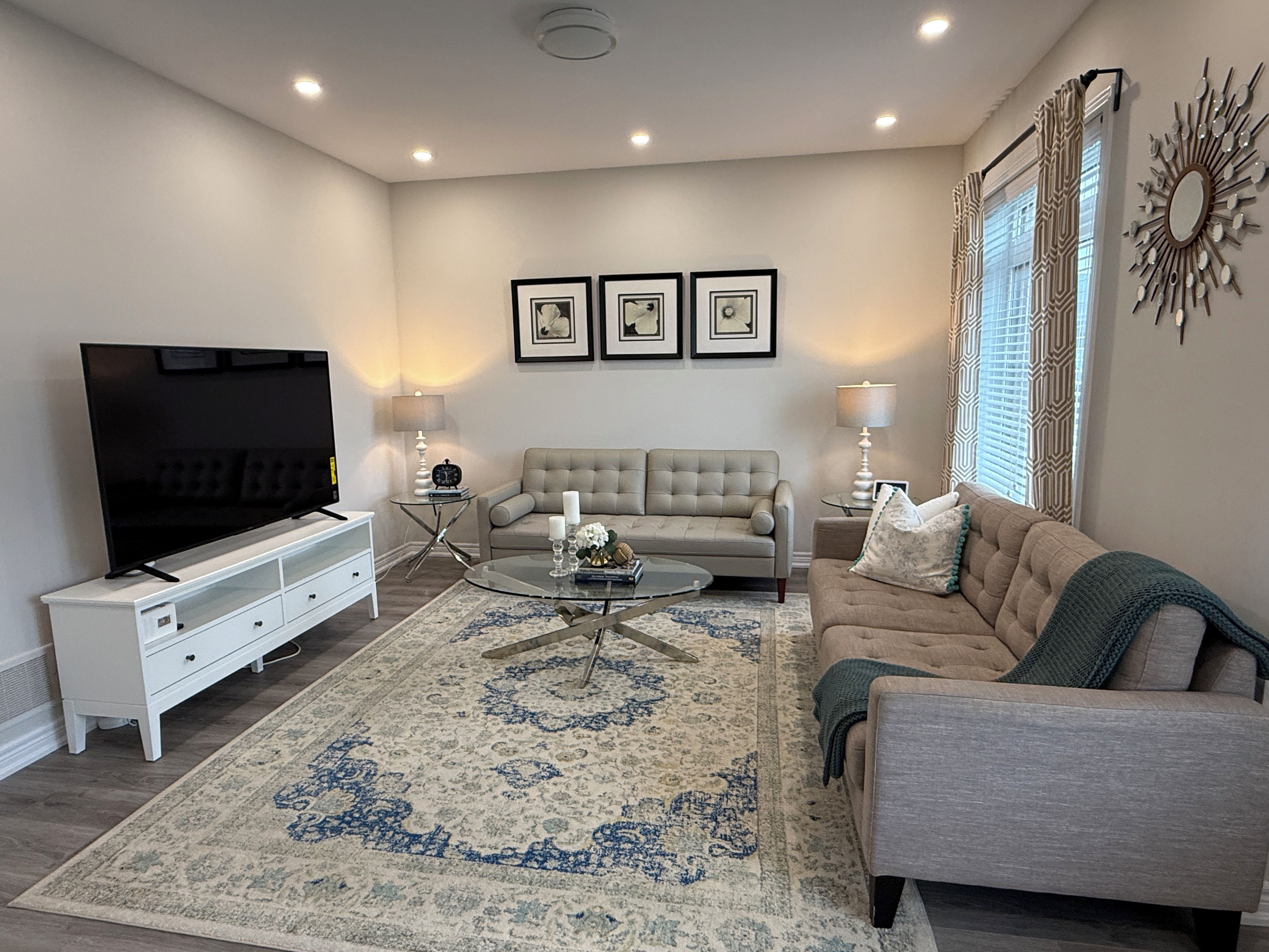 A living room with a flat-screen TV, a beige sofa, a coffee table, and a patterned rug.