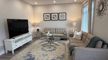 A living room with a flat-screen TV, a beige sofa, a coffee table, and a patterned rug.