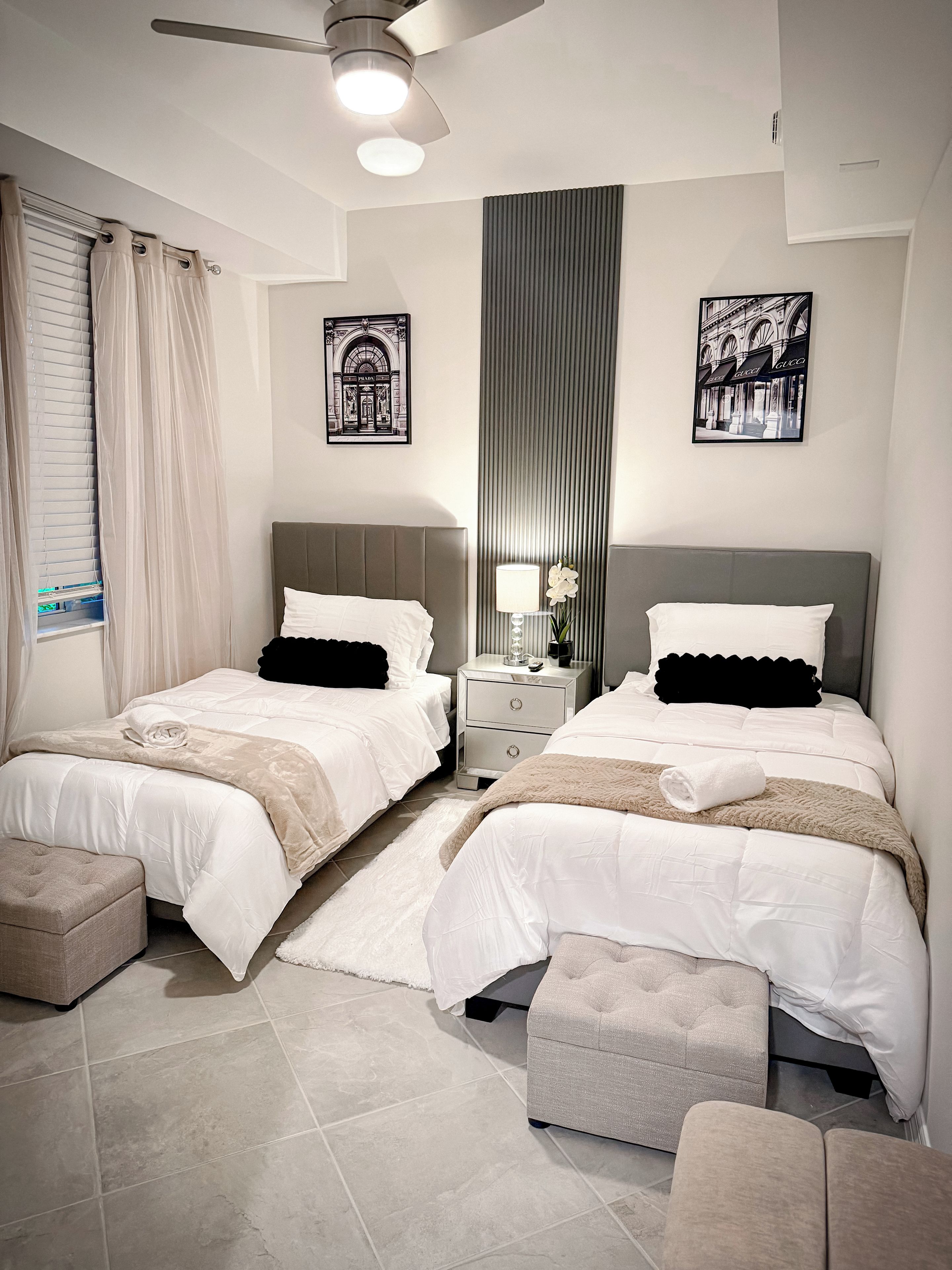 Une chambre d’hôtel avec deux lits, une table de chevet, une lampe et une grande fenêtre avec des rideaux.